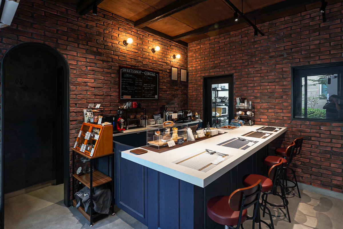 改修後の店内。赤茶色のレンガの壁と、白い天板に青い腰板のカウンター、赤い座面の椅子が並ぶ